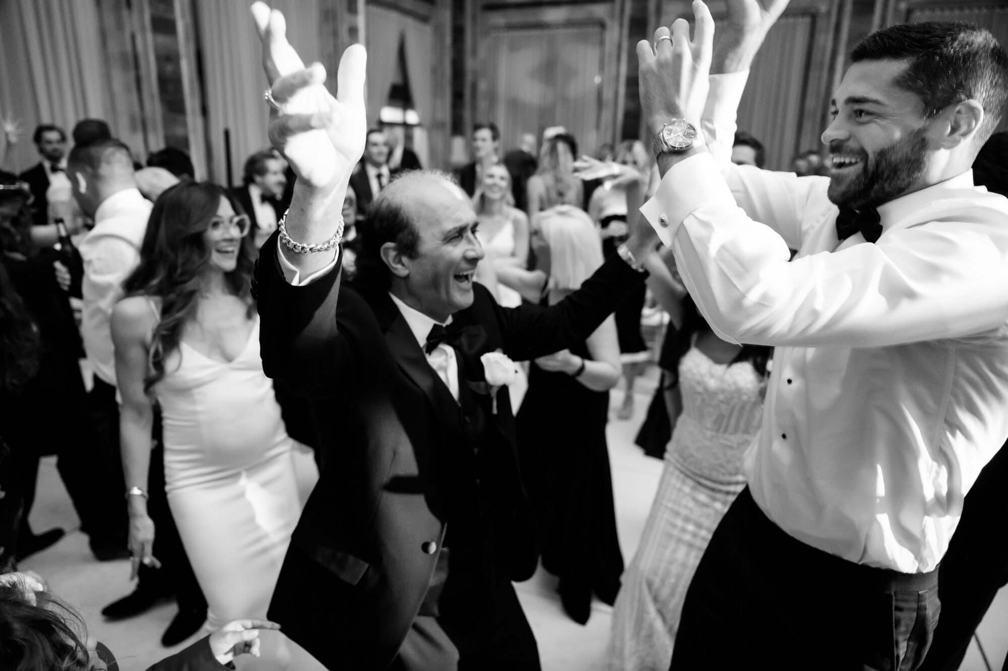 Black and white photo of guests cheering and throwing hands up on the dance floor