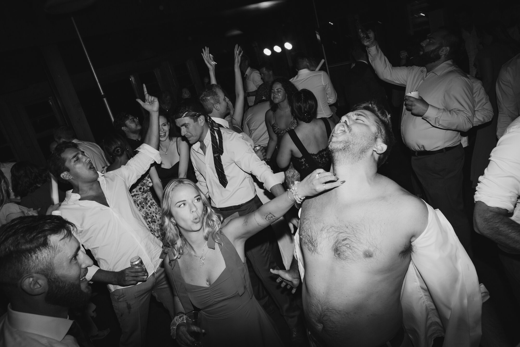 Black and white photo of a packed reception dance floor with a shirtless groomsman and bridesmaid mid-celebration