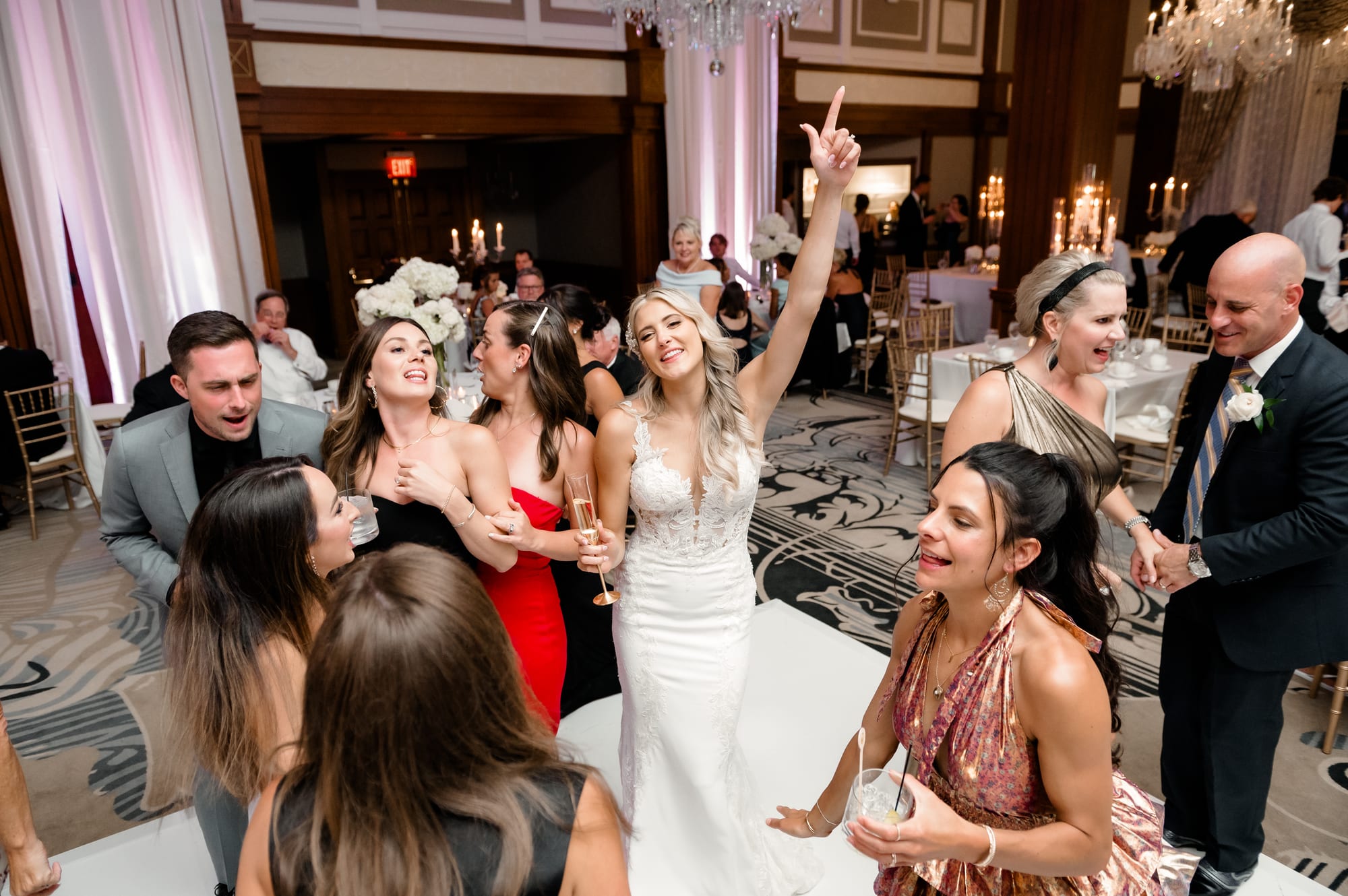 Bride raising her arm and singing on a packed Nemacolin ballroom dance floor surrounded by friends