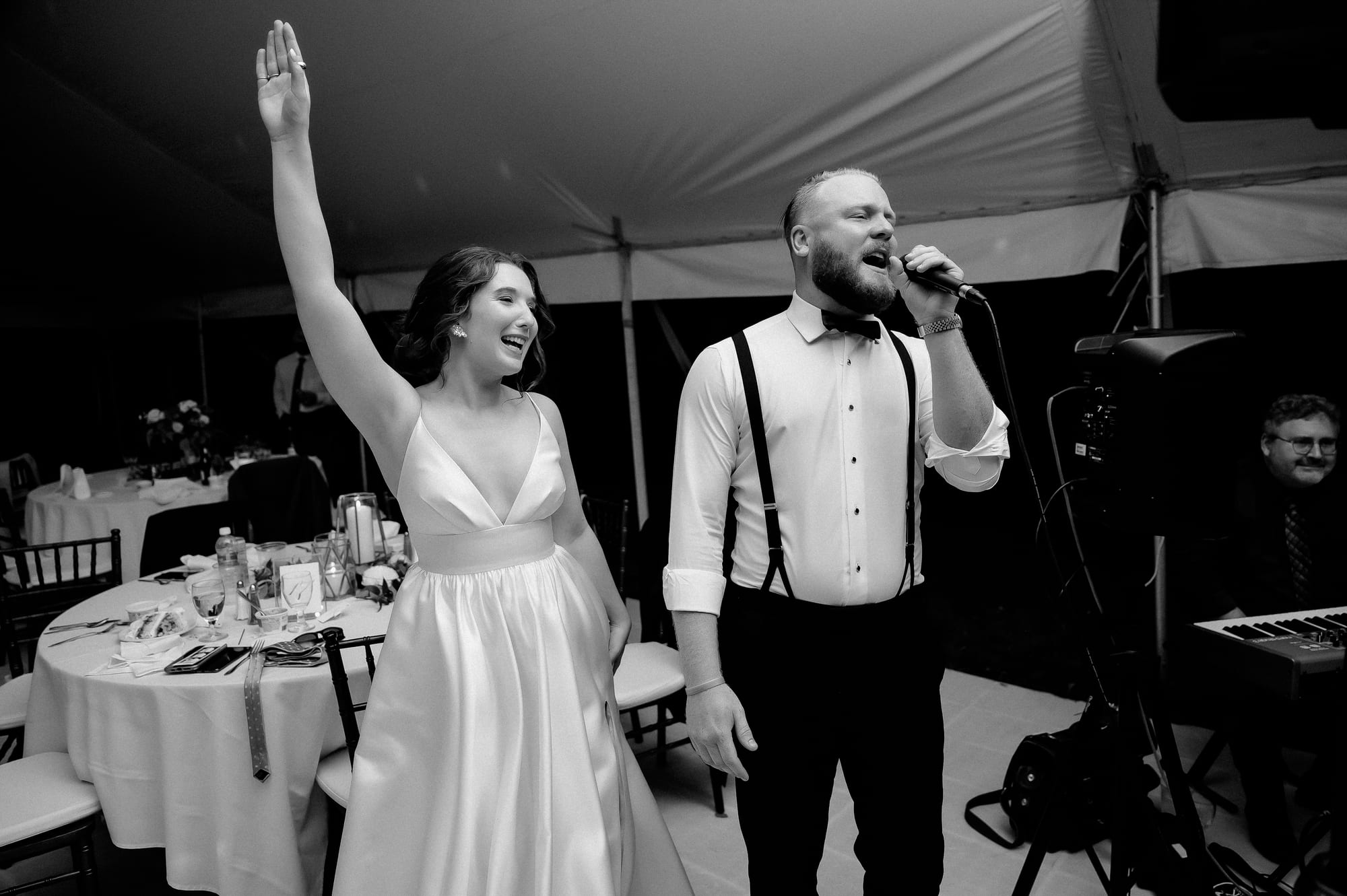 Bride raising her arm while the vocalist performs at a black-and-white tented private-residence reception