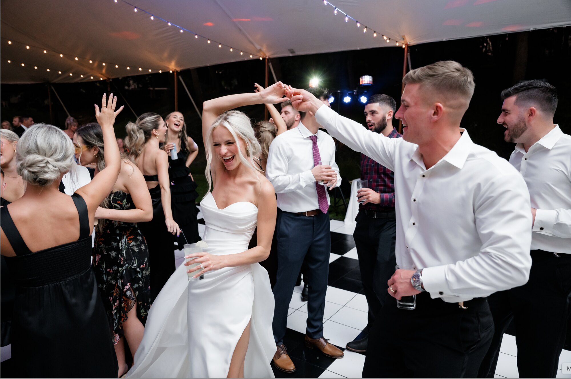 Bride dancing under string lights on a packed tented dance floor